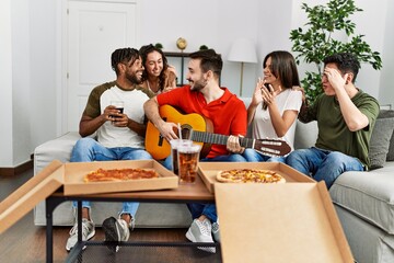Group of young friends having party eating italian pizza and playing classical guitar at home.