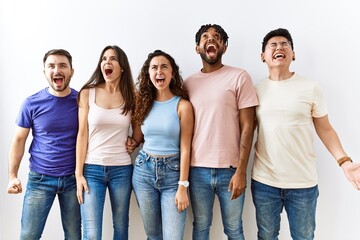Obraz premium Group of young people standing together over isolated background angry and mad screaming frustrated and furious, shouting with anger. rage and aggressive concept.