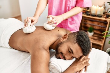 Obraz na płótnie Canvas Young african american man reciving herbal pouches thai massage at beauty center.