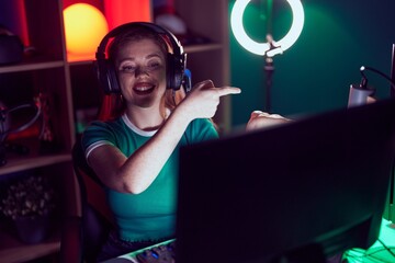 Redhead woman playing video games amazed and smiling to the camera while presenting with hand and...