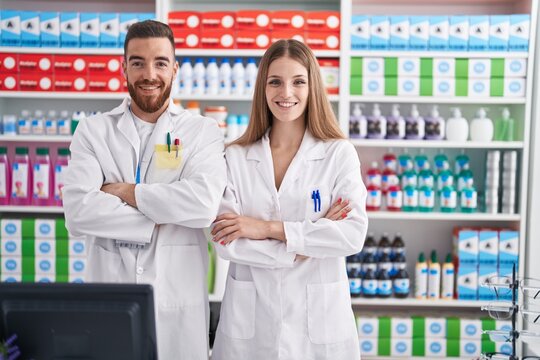 Man and woman pharmacists smiling confident standing with arms crossed gesture at pharmacy