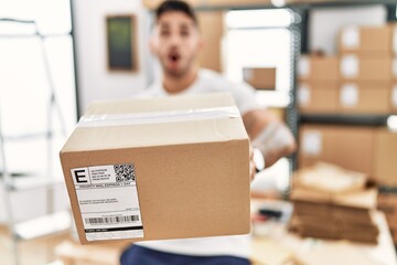 Young hispanic man working at small business ecommerce holding box afraid and shocked with surprise...