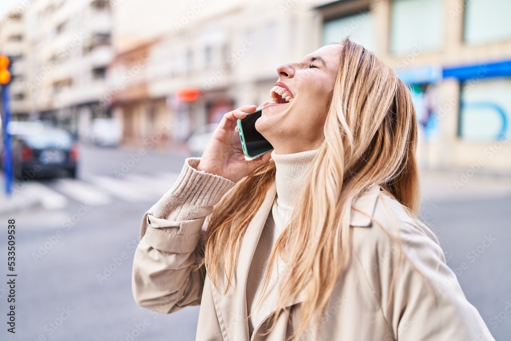 Canvas Prints Young blonde woman smiling confident talking on smartphone at street