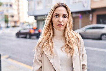 Young blonde woman standing with serious expression at street