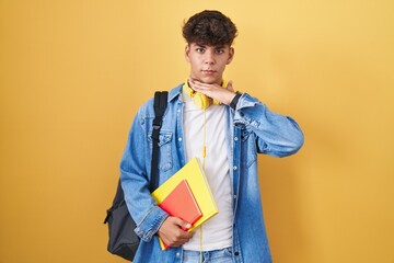 Hispanic teenager wearing student backpack and holding books cutting throat with hand as knife, threaten aggression with furious violence