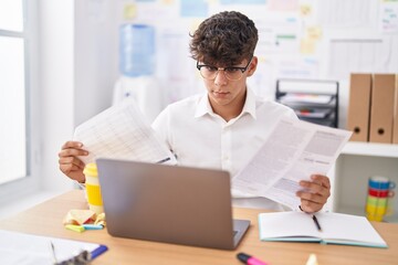 Young hispanic teenager business worker using laptop reading document at office