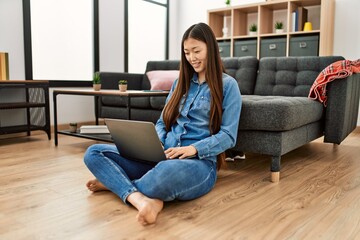 Young chinese girl using laptop sitting on the floor at home. © Krakenimages.com