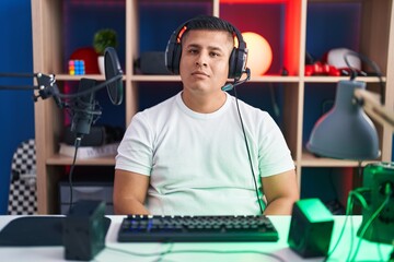 Young hispanic man playing video games relaxed with serious expression on face. simple and natural looking at the camera.