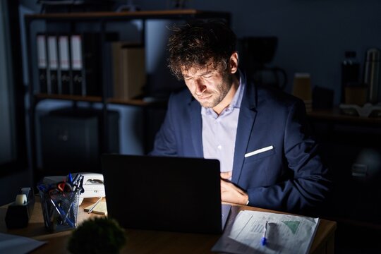 Hispanic young man working at the office at night with hand on stomach because indigestion, painful illness feeling unwell. ache concept.