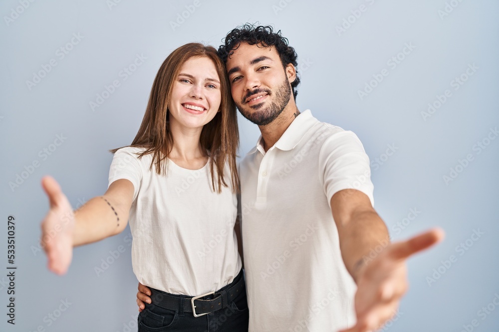 Canvas Prints Young couple wearing casual clothes standing together looking at the camera smiling with open arms for hug. cheerful expression embracing happiness.