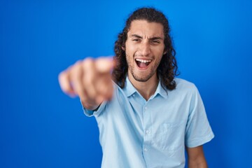 Young hispanic man standing over blue background pointing displeased and frustrated to the camera, angry and furious with you