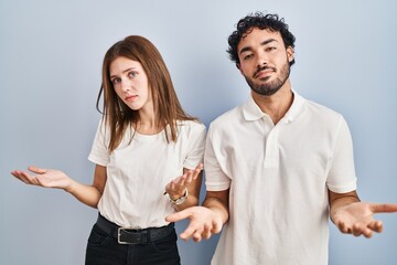 Young couple wearing casual clothes standing together clueless and confused with open arms, no idea concept.