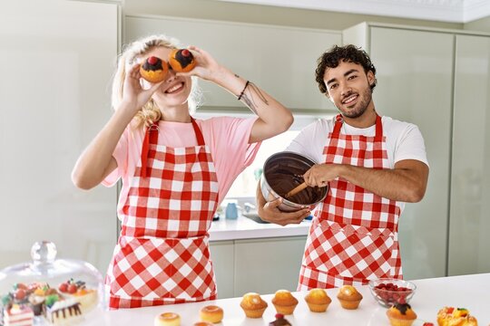 Young couple smiling happy cooking sweets holding pumpkin on eyes at kitchen.