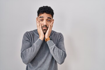 Hispanic man with beard standing over white background tired hands covering face, depression and...