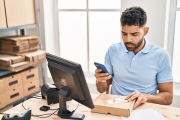 Young hispanic man ecommerce business worker using smartphone at office