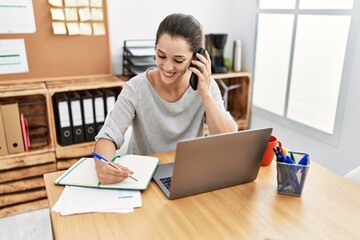 Young hispanic woman working and talking on the smartphone at office