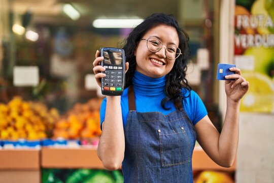 Young chinese woman employee holding data phone and credit card at fruit store