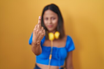 Hispanic young woman standing over yellow background showing middle finger, impolite and rude fuck...