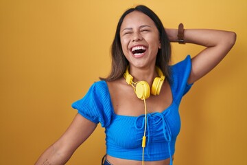 Hispanic young woman standing over yellow background dancing happy and cheerful, smiling moving casual and confident listening to music