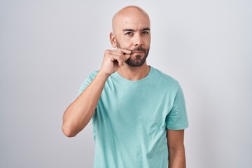 Middle age bald man standing over white background mouth and lips shut as zip with fingers. secret...