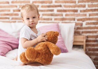Adorable toddler sitting on bed playing with teddy bear at bedroom