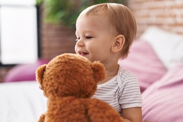 Adorable toddler playing with teddy bear sitting on bed at bedroom