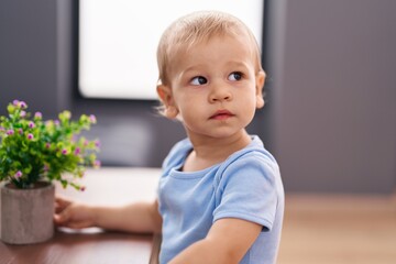 Adorable toddler holding plant with relaxed expression at home