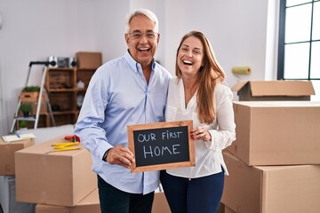 Middle age hispanic couple moving to a new home holding banner smiling and laughing hard out loud because funny crazy joke.