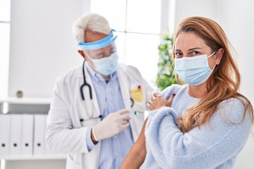 Middle age man and woman doctor wearing medical mask vaccinating patient at clinic