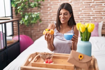 Young beautiful hispanic woman having gift breakfast sitting on bed at bedroom