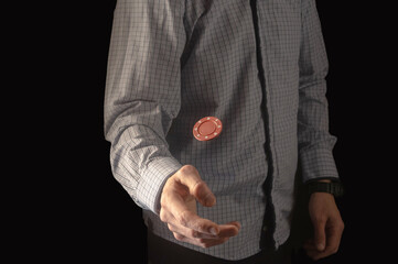 A man in a shirt flips a red chip. Bet on red. Poker chip in the air.