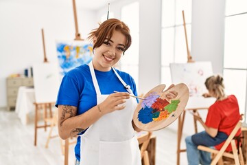 Two artist student women smiling happy painting at art school. Girl holding palette and paintbrush.