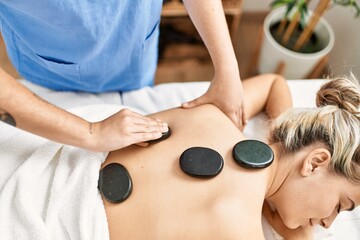 Woman couple having back treatment using hot black stones at beauty center