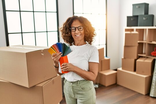 Middle age hispanic woman smiling confident holding paint tester at new home