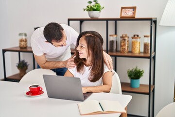 Middle age man and woman couple hugging each other working sitting on table at home