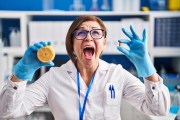 Middle age hispanic woman working at scientist laboratory making vitamin angry and mad screaming...