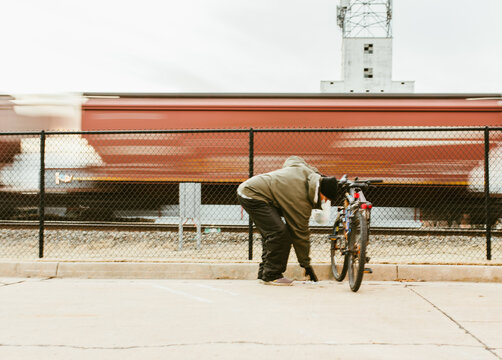 Homeless Man With A Bike Collecting Cans Outdoors Near The Train Tracks. Social Problems Of Big Modern Cities.