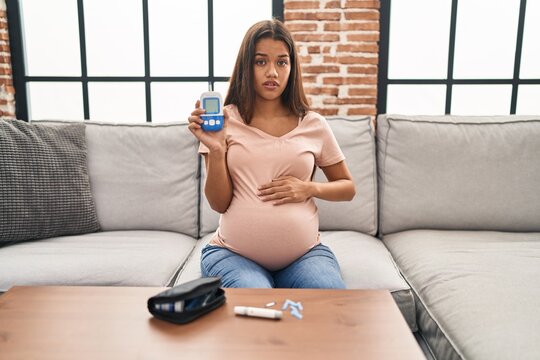 Young pregnant woman checking blood sugar clueless and confused expression. doubt concept.
