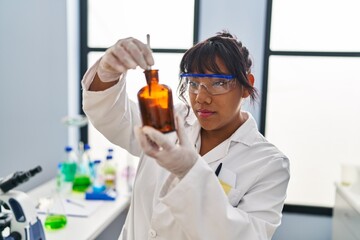 Young beautiful latin woman scientist holding plant with tweezers on bottle at laboratory