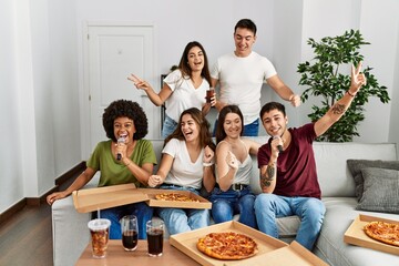 Group of young friends having party eating italian pizza and singing song at home.