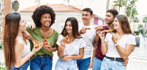 Group of young friends smiling happy eating pizza standing at the city.