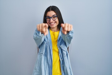 Young hispanic woman standing over blue background pointing to you and the camera with fingers, smiling positive and cheerful