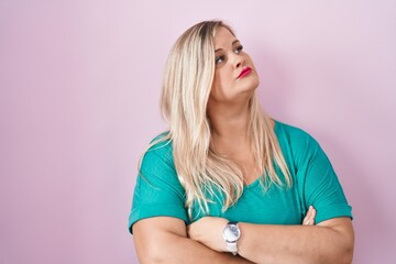 Caucasian plus size woman standing over pink background looking to the side with arms crossed...