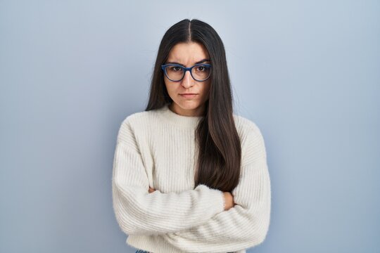 Young hispanic woman wearing casual sweater over blue background skeptic and nervous, disapproving expression on face with crossed arms. negative person.