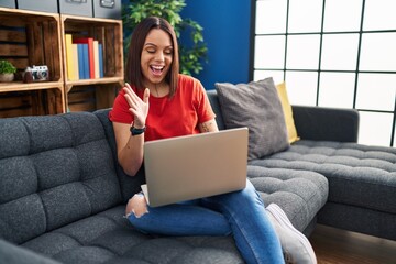 Young hispanic woman using laptop at home celebrating victory with happy smile and winner expression with raised hands