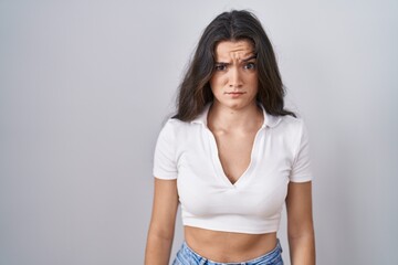 Young teenager girl standing over white background skeptic and nervous, frowning upset because of...