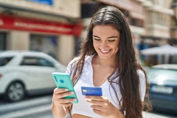 Young hispanic woman using smartphone and credit card at street