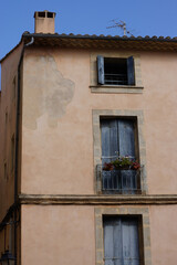 Fototapeta na wymiar Altes südfranzösisches Wohnhaus, okzitanischer Baustil. Die Fassade ist in warmen, hellen Erdfarben gehalten, die Fenster schmal und hoch (abgesehen vom obersten Stockwerk), die Fensterländen blau. 