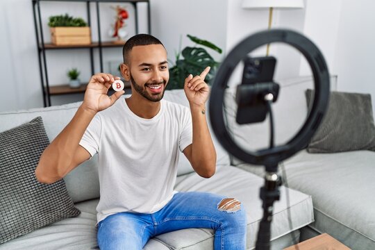 African american man recording vlog tutorial about bitcoin with smartphone at home smiling happy pointing with hand and finger to the side