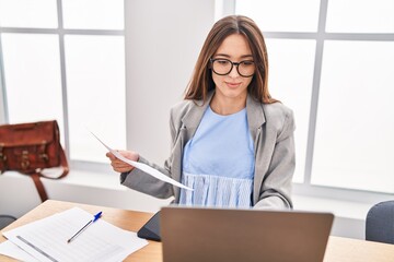 Young beautiful hispanic woman business worker using laptop reading document at office